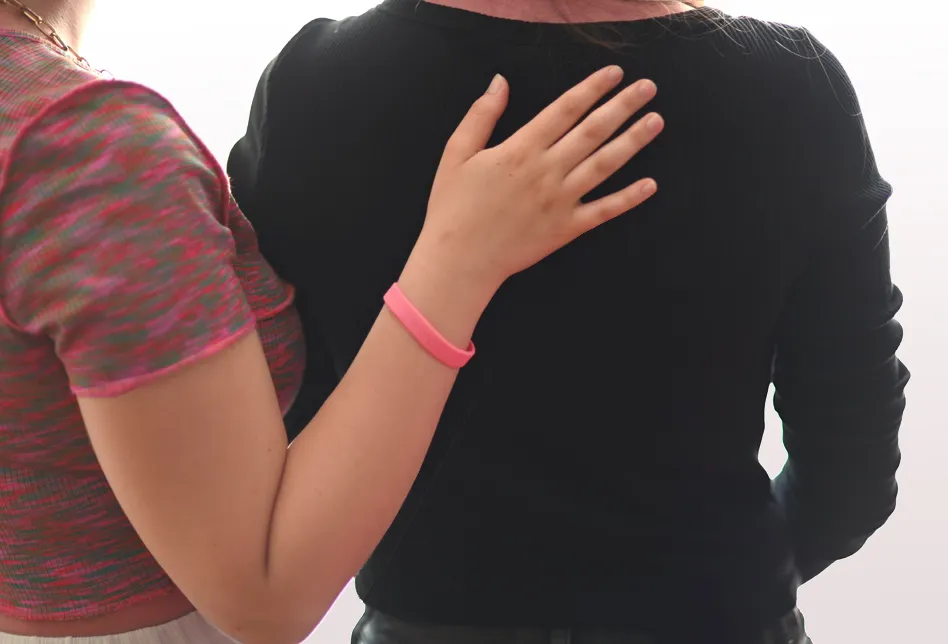 Zwei Menschen von hinten fotografiert. Die eine Person hält der anderen stützend die Hand an den Rücken.
