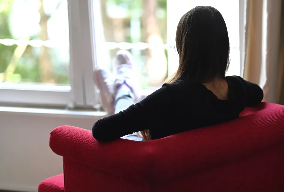 Ein Mensch mit langen Haaren sitzt mit dem Rücken zum Betrachtenden in einem roten Sessel