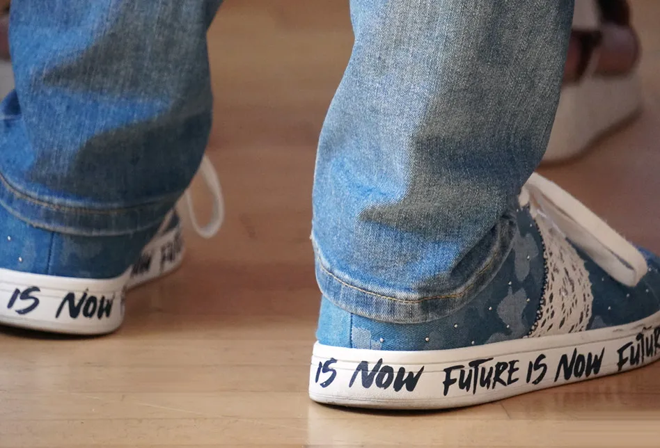 Eine Person trägt Jeans und Turnschuhe auf deren Sohlen mit Edding 'The future is now' geschrieben steht.